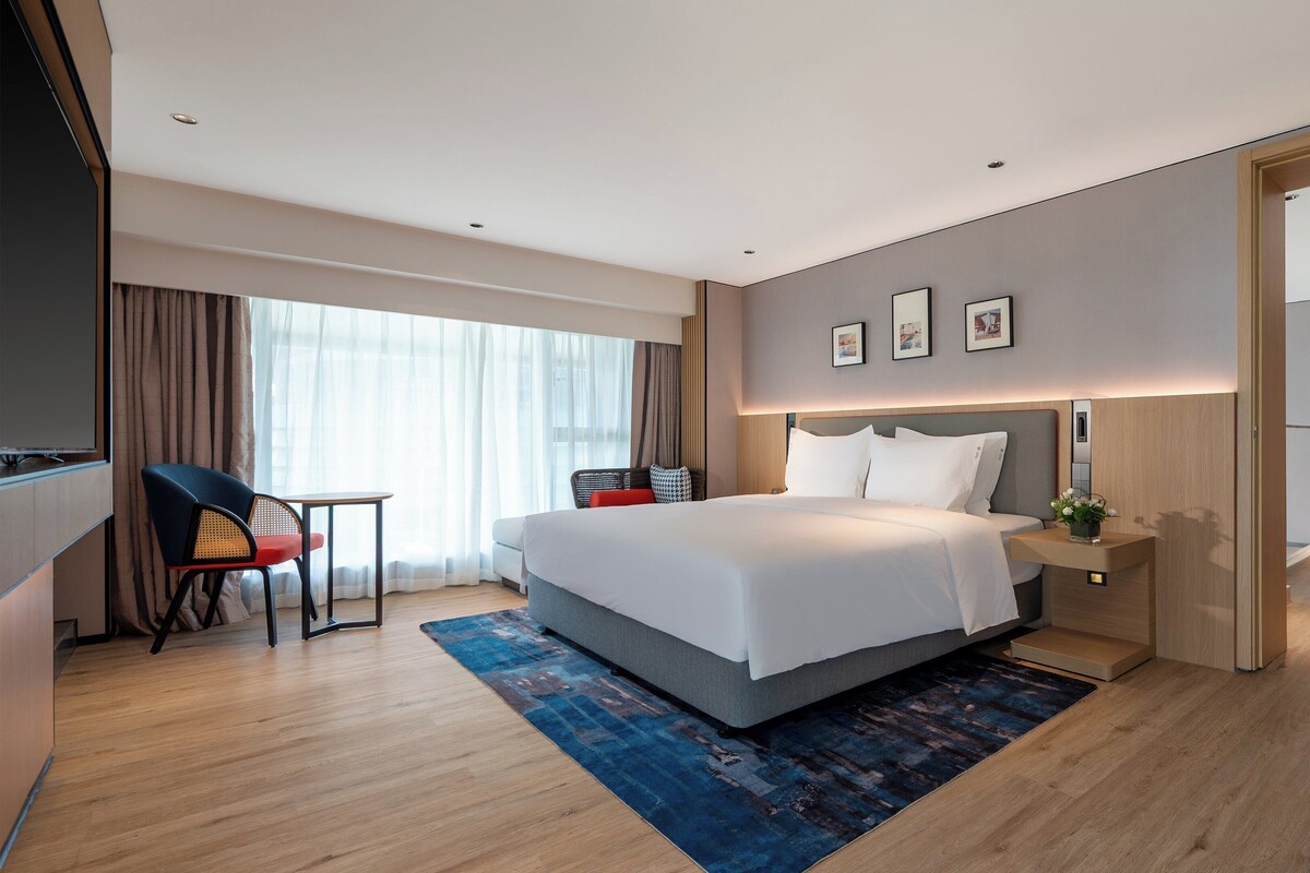 A modern hotel room with a large bed, a desk with a chair, a small table, and a sofa.