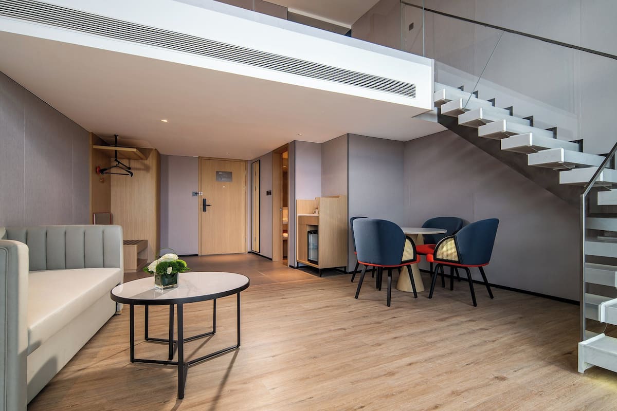 A modern interior with a staircase, a sofa, a table with chairs, and a small kitchenette.