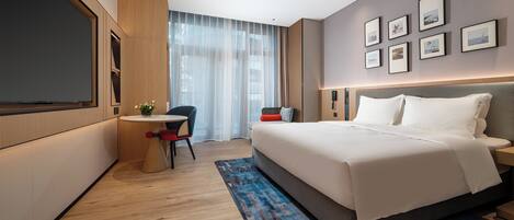 Quarto de hotel moderno com uma cama grande, uma escrivaninha com cadeira, televisão de tela plana e uma grande janela com cortinas finas.