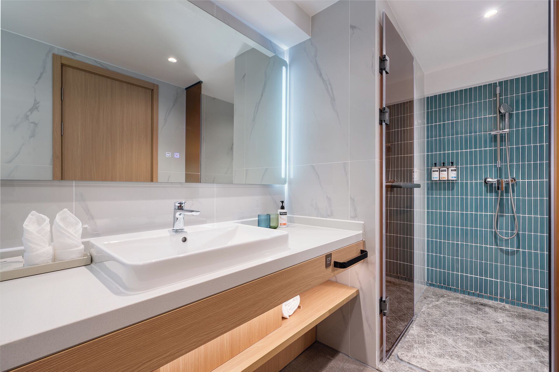 A modern bathroom with a white sink, a mirror, and a shower area with blue tiles.