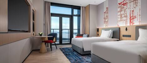 A hotel room with two beds, a desk, and a large window offering a city view.