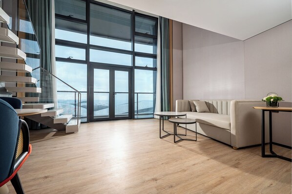 A modern living room with a staircase, a sofa, a small table, and a view through large windows. - Holiday Inn Express Haikou Intl Duty Free City by IHG (Haikou)
