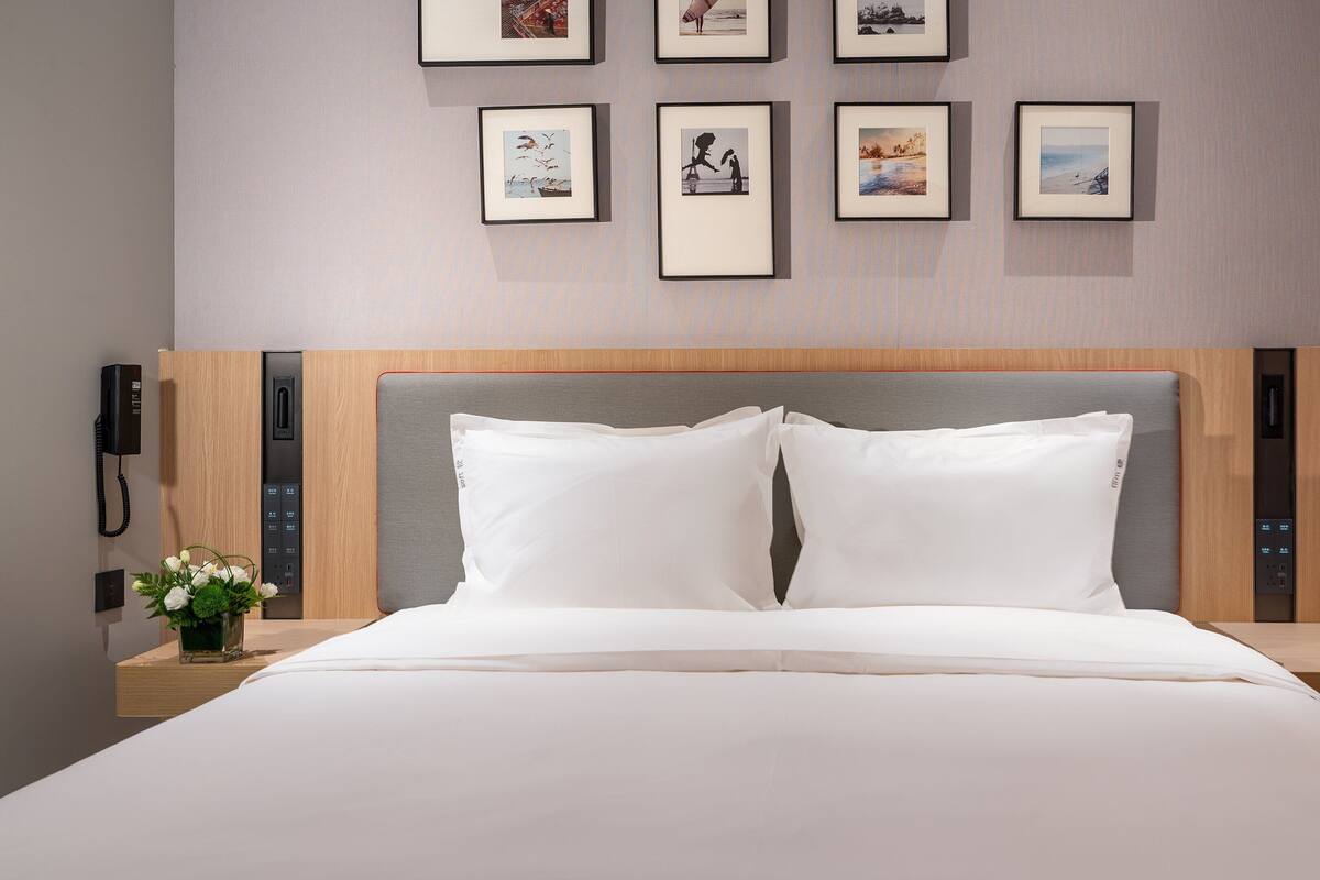 A hotel room with a large bed, a wooden headboard, a bedside table with a phone, and framed pictures on the wall.
