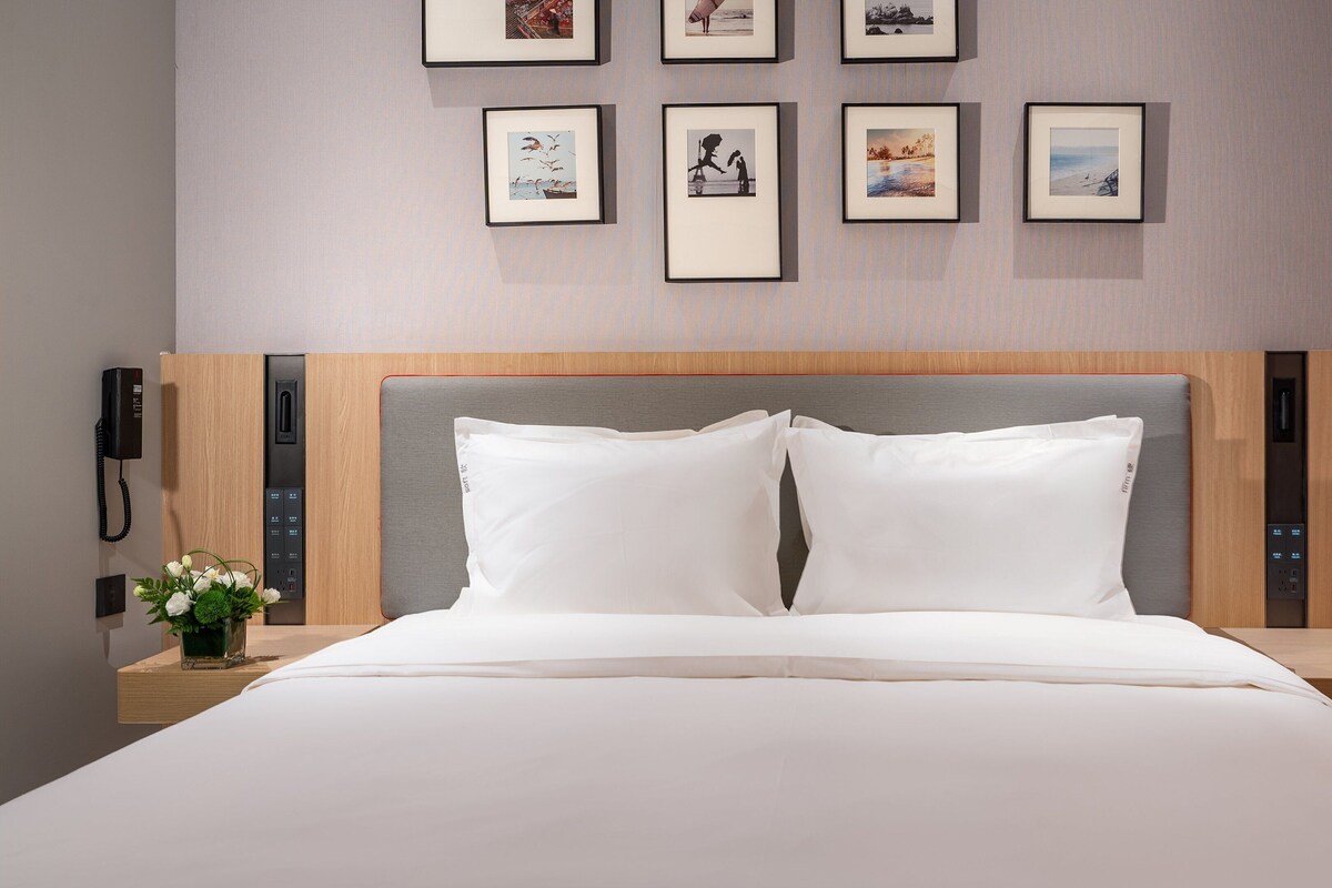 A hotel room with a large bed, a wooden headboard, a bedside table with a phone, and framed pictures on the wall.