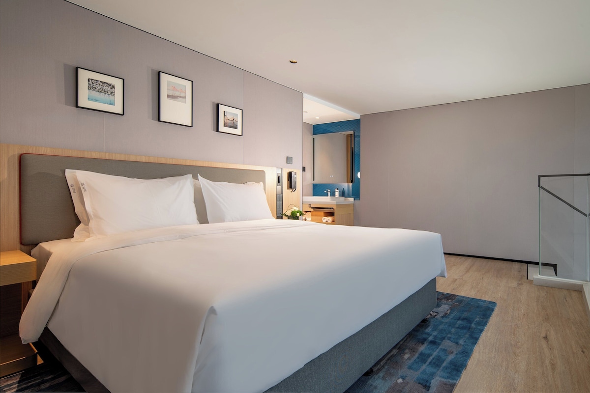 A modern hotel room with a large bed, a bedside table, a mirror, and a staircase.