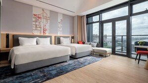 A modern hotel room with two beds, a large window with a city view, a small table with a vase, and a red chair. - Holiday Inn Express Haikou Intl Duty Free City by IHG (Haikou)