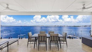 A dining area with a view of the sea, featuring a table and chairs, a bench, and ceiling fans. - 319 Bay and Beach Blessing: Bay Front Pool Home w/ Gulf Views (Fort Myers Beach)
