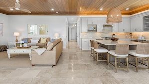 A spacious living room with a sofa, coffee table, and a dining area with chairs and a kitchen in the background. - 319 Bay and Beach Blessing: Bay Front Pool Home w/ Gulf Views (Fort Myers Beach)