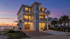 A multi-story waterfront property with balconies, a garage, and a well-lit entrance. - 319 Bay and Beach Blessing: Bay Front Pool Home w/ Gulf Views (Fort Myers Beach)