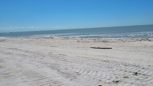 Una playa arenosa con huellas y un trozo de madera a la orilla.