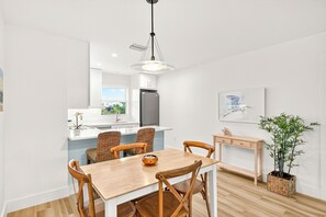 A modern kitchen with white cabinets, a stainless steel refrigerator, and a dining area with a wooden table and chairs.