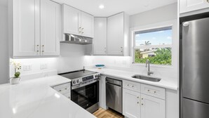 Una cocina moderna con armarios blancos, electrodomésticos de acero inoxidable y una ventana que ofrece vistas al exterior.