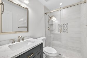 A modern bathroom with a marble sink, a toilet, and a glass-enclosed shower.