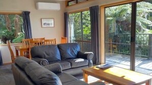 A modern living room with a black leather sofa, wooden coffee table, and a large sliding glass door leading to a balcony. - Pukawa Villas (Formerly Oreti Village Resort) (Pukawa)