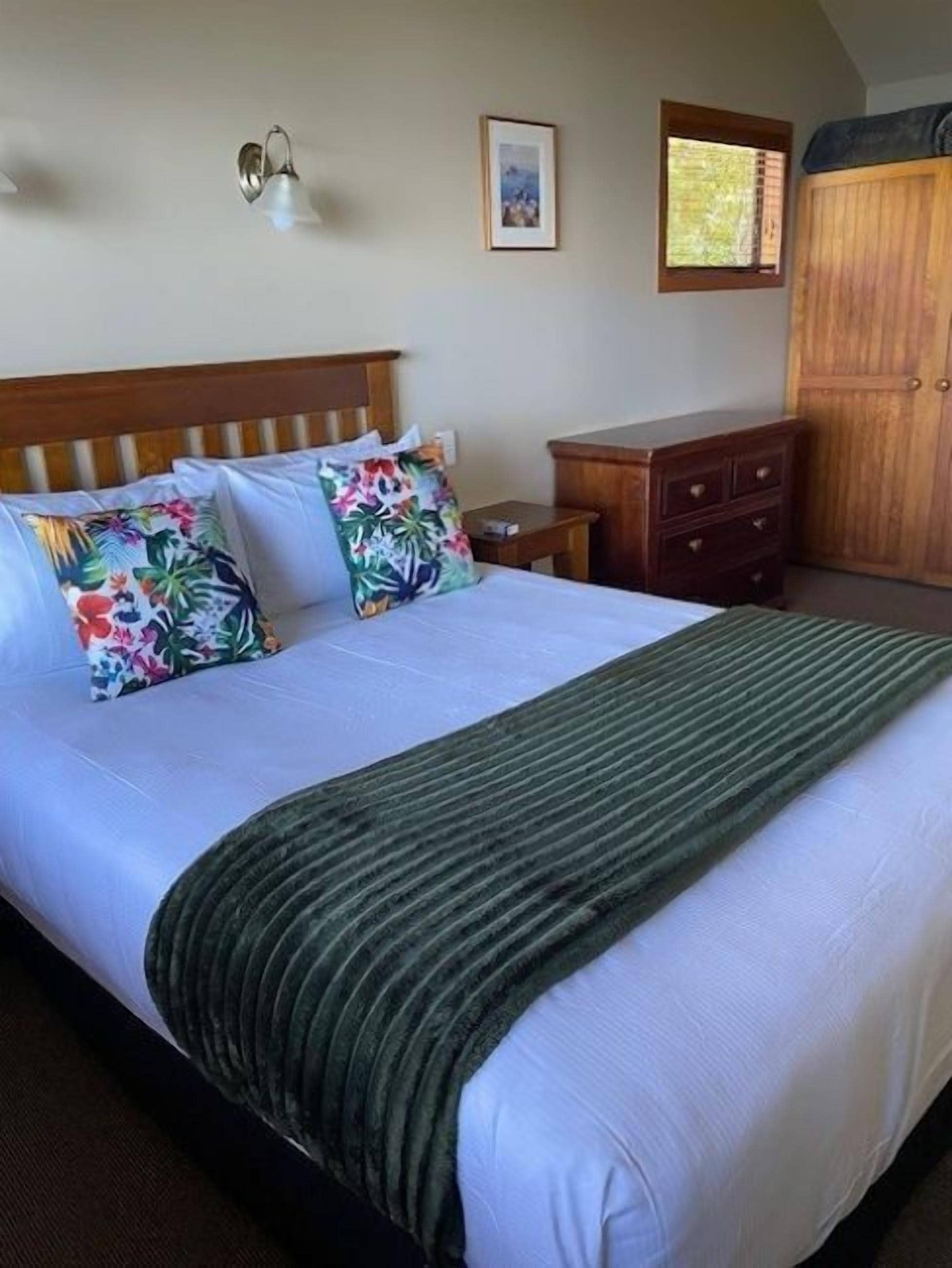 A neatly made bed with a striped blanket, a wooden headboard, and two floral pillows.