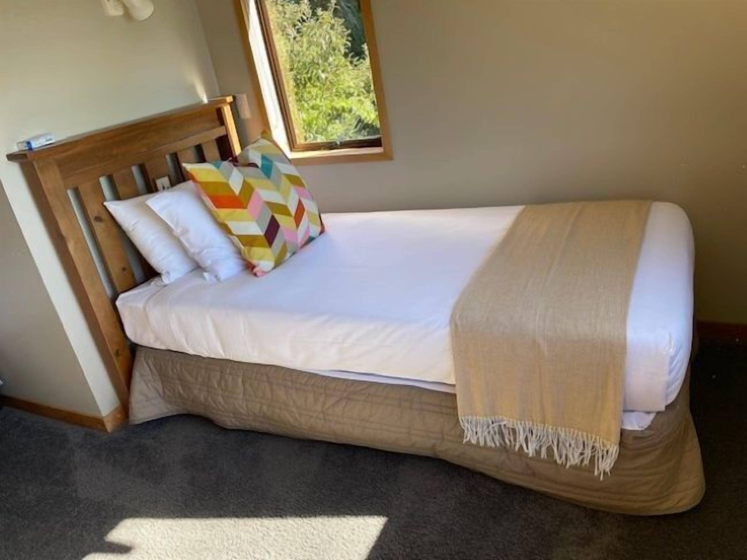 Un lit simple avec une tête de lit en bois, du linge de lit blanc et un coussin coloré.