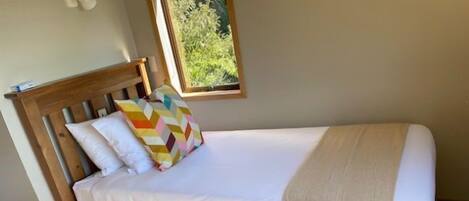 Un lit simple avec une tête de lit en bois, du linge de lit blanc et un coussin coloré.