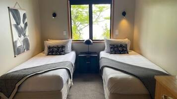 Une chambre avec deux lits simples, une table de chevet, une lampe et une fenêtre donnant sur des arbres.