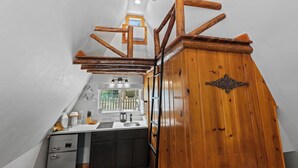 A compact kitchen with a wooden staircase, a small window with a view of a white fence, and a sink with modern fixtures. - Timber Lodge Cabins 25 (Colorado Springs)
