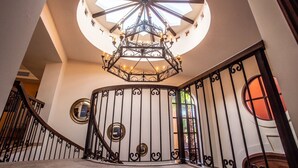 A grand staircase with a wrought iron railing, a decorative chandelier, and a skylight.