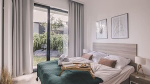 Ein modernes Hotelzimmer mit einem großen Bett, Blick auf Grünfläche und zwei gerahmten Kunstwerken an der Wand.
