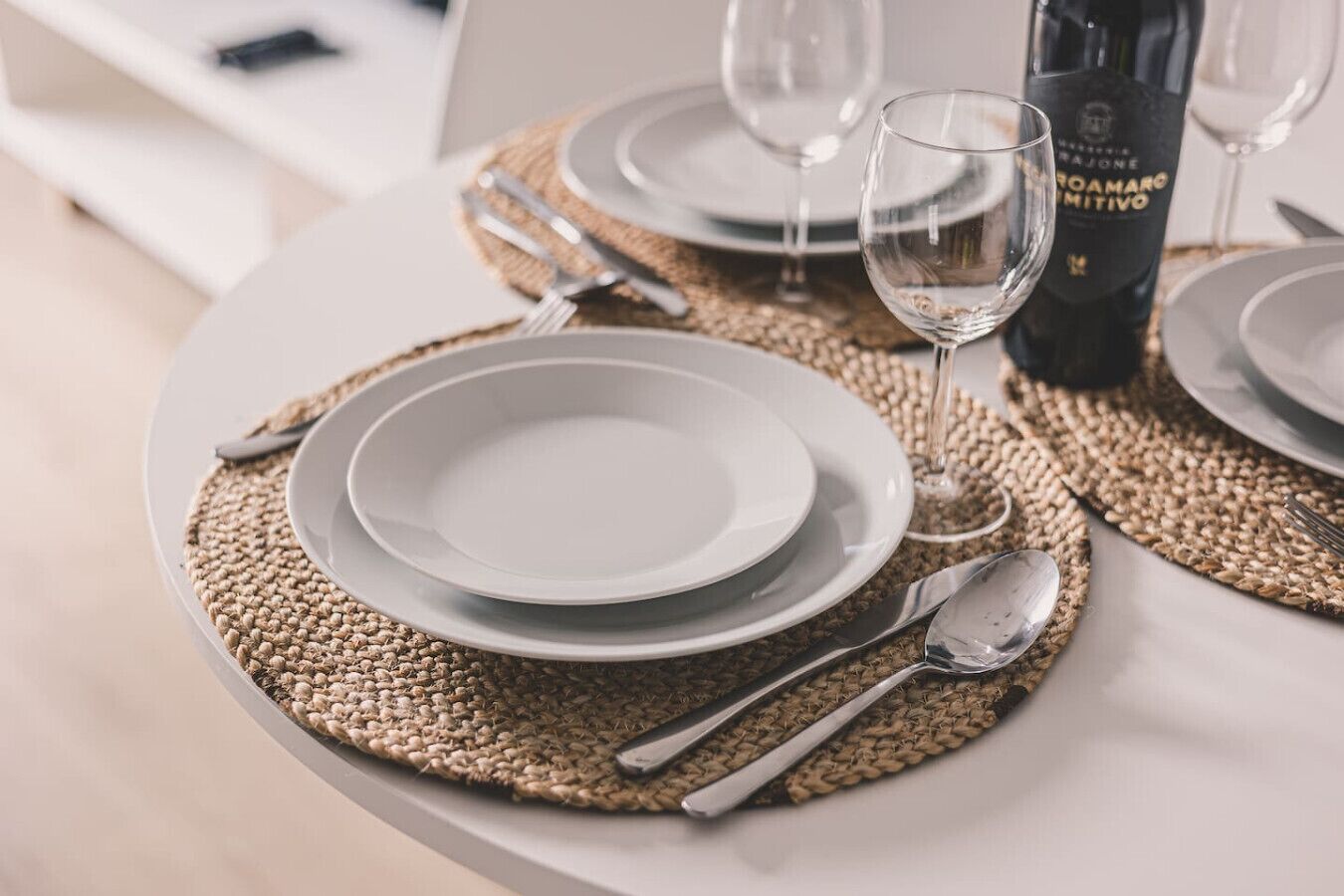Une table à manger élégamment dressée, avec de l’argenterie, des assiettes blanches et une bouteille de vin.