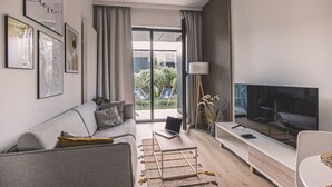 Ein modernes Wohnzimmer mit grauem Sofa, einem Flachbildfernseher, einem Couchtisch und einem großen Fenster mit Vorhängen.