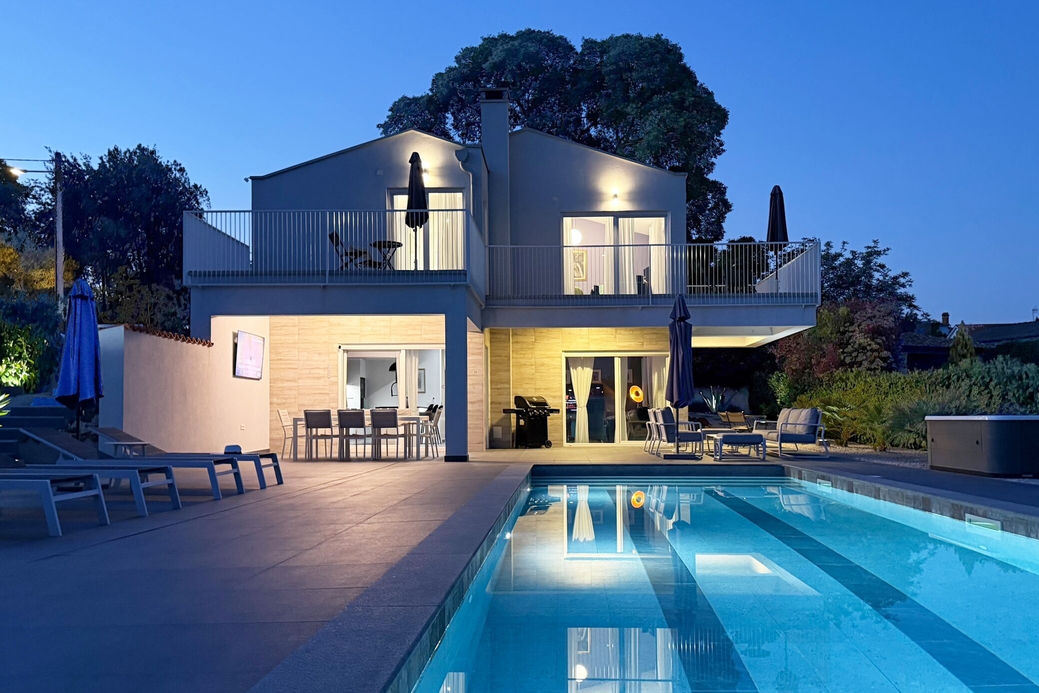 Une maison moderne à deux étages dotée d’une piscine, d’un espace salon extérieur et d’un balcon.