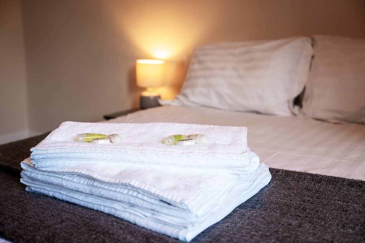 A neatly made bed with a stack of folded towels and a bottle of lotion on it.
