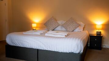 A neatly made bed with white linens and floral-patterned pillows, flanked by two bedside lamps on a dark nightstand.
