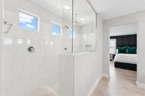 Een moderne badkamer met witte tegels, een glazen douchecabine en een zichtbaar raam.