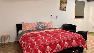 Un dormitorio ordenado con cama, una silla, un taburete pequeño y un aire acondicionado instalado en la pared.