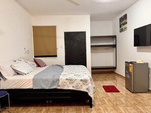 A small, well-lit bedroom with a bed, a wardrobe, a desk, and a refrigerator. - ESPADA LODGE Studio 3.3 (Somanya)