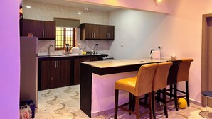 A modern kitchen with dark wooden cabinets, a marble countertop, and a built-in island with bar stools. - ESPADA LODGE Studio 3.3 (Somanya)