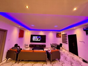 A modern living room with a flat-screen TV, a sofa, and a dining area. - ESPADA LODGE Studio 3.3 (Somanya)