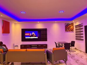 Ein modernes Wohnzimmer mit Flachbildfernseher, bequemen Sitzmöglichkeiten und einer Wanddekoration.