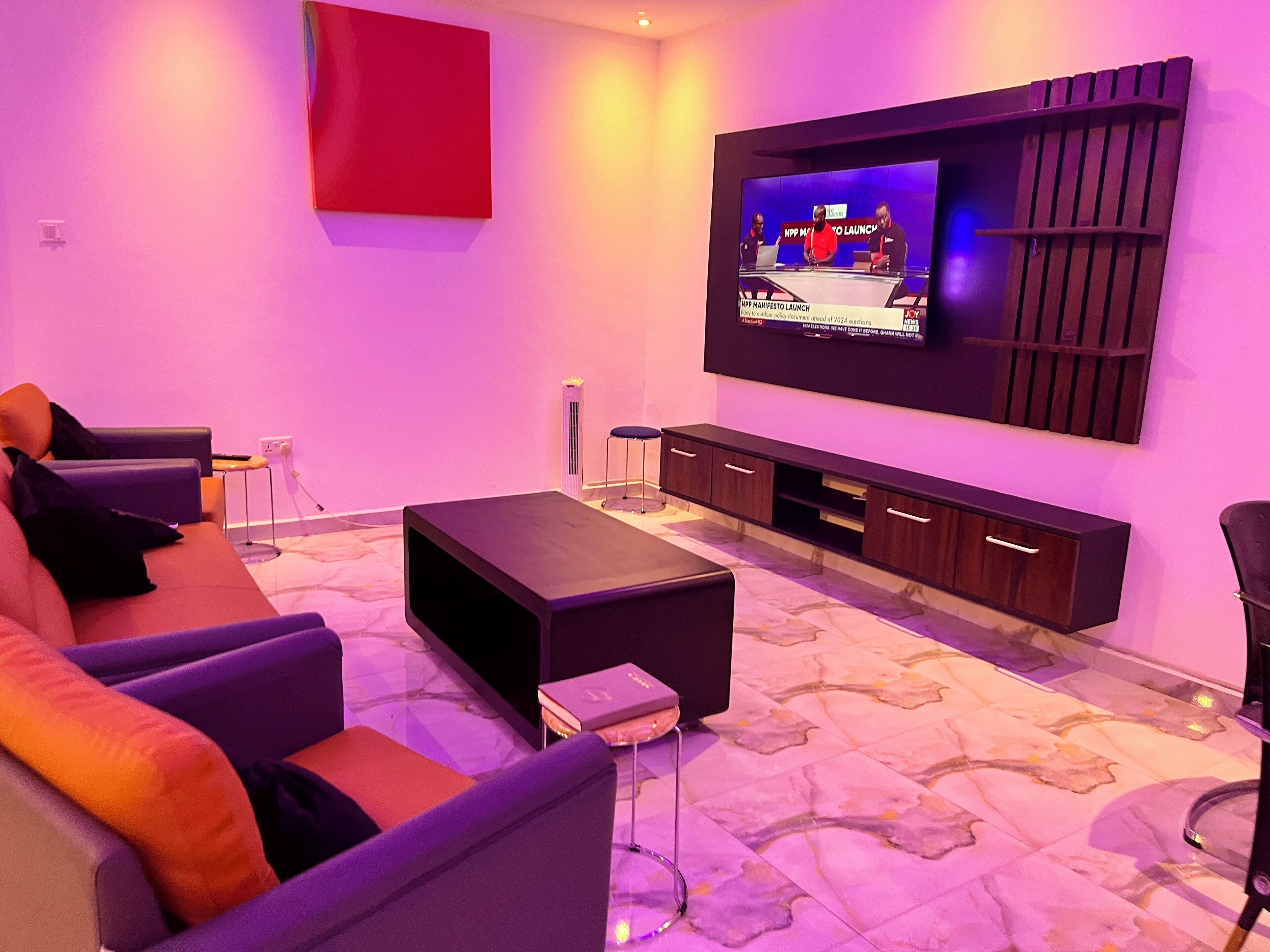 Een moderne woonkamer met een flatscreen televisie aan de muur, een donker houten dressoir, een bank met kussens en een kamerkleed met een patroon.