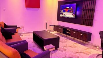 Een moderne woonkamer met een flatscreen televisie aan de muur, een donker houten dressoir, een bank met kussens en een kamerkleed met een patroon.