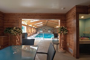 A wooden cabin with a pool, furnished with wicker chairs and a table, and decorated with string lights.