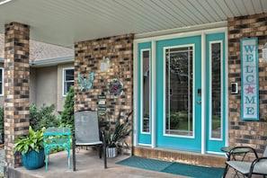 A building entrance with a brick facade, a teal-colored door, and a welcome sign.