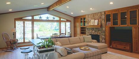 A spacious living room with a sectional sofa, a dining area with a table and chairs, and a stone fireplace.