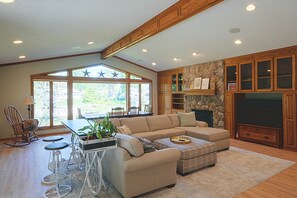 A spacious living room with a sectional sofa, a dining area with a table and chairs, and a stone fireplace.