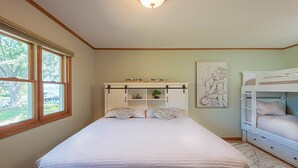 A bedroom with a bed, a window, a shelf with decorative items, a bunk bed, and a wall art piece.