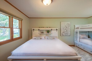 A bedroom with a bed, a window, a shelf with decorative items, a bunk bed, and a wall art piece.
