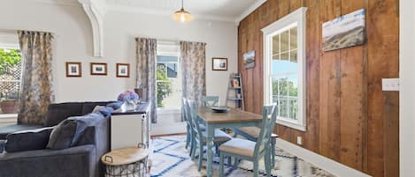 Een eethoek met een houten tafel en stoelen, een kamerbreed tapijt en uitzicht door een raam.