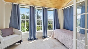 Ein Zimmer mit Holzboden, großen Fenstern mit Vorhängen, einem weißen Sofa, einem Bett und einer Glastür.