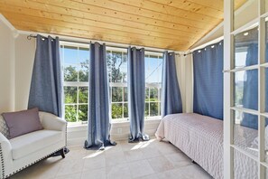 A room with a wooden ceiling, large windows with curtains, a white sofa, a bed, and a glass door. - Peaceful Historic Home Steps from Main Street with Porch & Patio (Angels Camp)