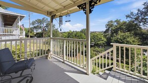 Eine überdachte Veranda mit weißer Holzvertäfelung, einer Bank und Blick auf Grünflächen sowie ein Gebäude im Hintergrund.