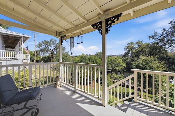 A covered porch with a white railing, a bench, and a view of greenery and a building in the background.
