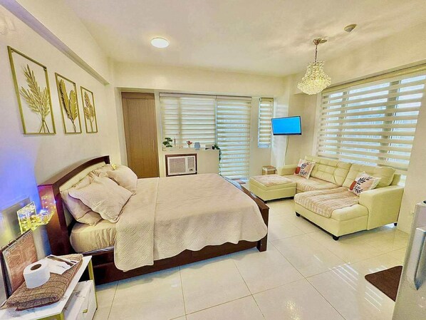A bedroom with a bed, a TV, a sofa, and a desk with a lamp.